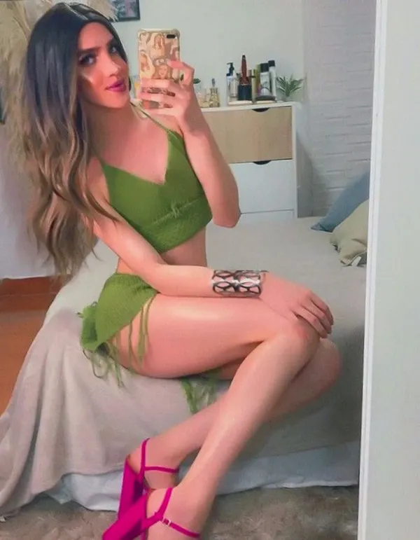 Woman in green outfit taking mirror selfie on bed