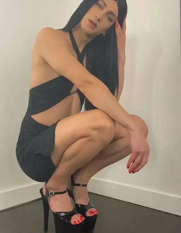 Woman squatting in black dress and platform heels
